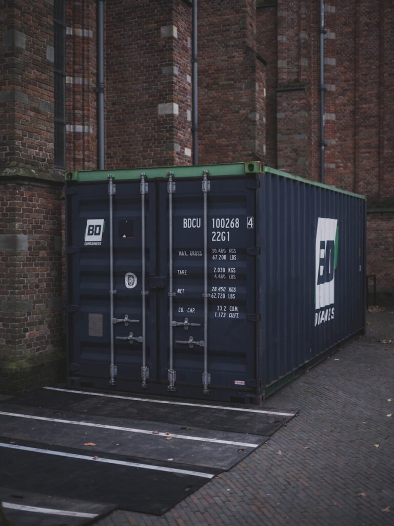 Seecontainer als Sachinvestition: Warum Hamburger Unternehmen statt mieten lieber kaufen Dark shipping container parked next to brick building.
